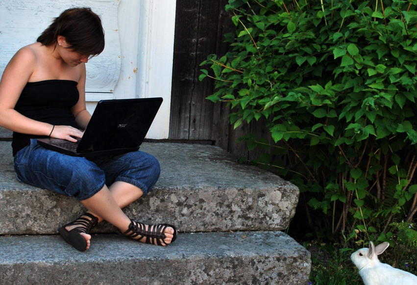 En tjej sitter på stentrappan utanför Ystegårn med en laptop i knäet och en vit kanin som sällskap.