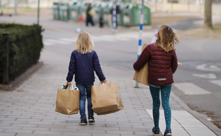 Två barn som går med fyllda papperskassar till återvinningsstation