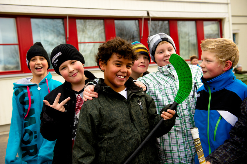 En grupp barn står framför ett fritidshem. En av dem har en innebandyklubba i sina händer. En annan visar vinnartecknet med sina fingrar.