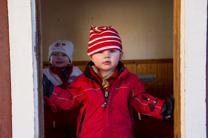 Två små barn står med ytterkläderna på sig i en dörröppning.