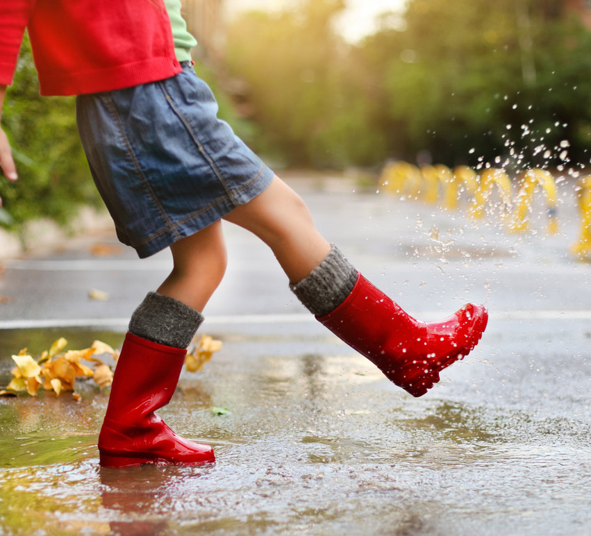 Barn med röda stövlar sparkar i en regnpöl