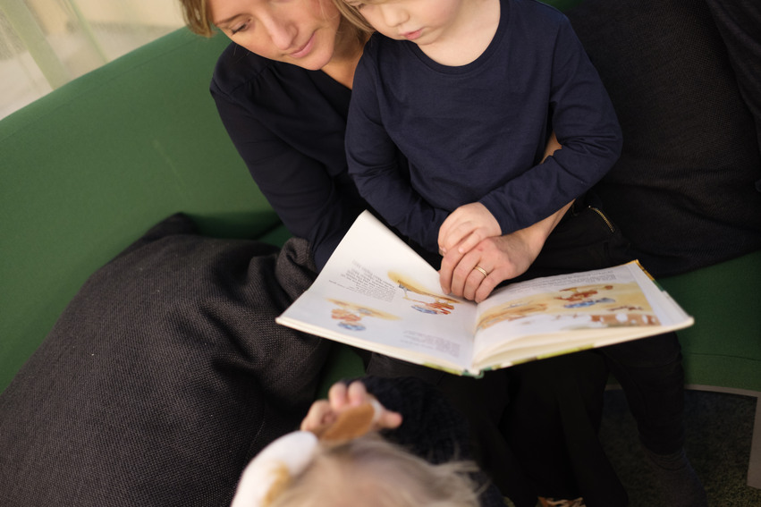 Mamma läser med sitt barn ur en barnbok som de håller framför sig.
