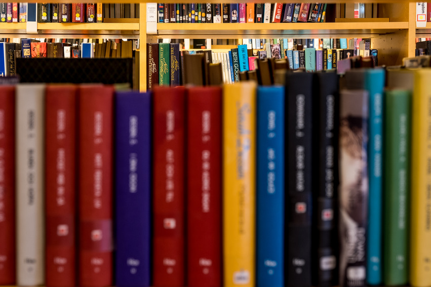 Närbild på en gulmålad bokhylla fylld med böcker i olika färger.