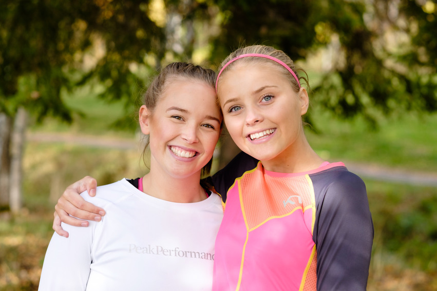 Närbild på två yngre tjejer på Kärleksstigen i Hudiksvall. En av tjejerna har ett rosa modem i håret, hon har lagt sin arm runt den andra tjejen. Båda ler
