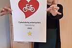 Person står och håller i diplomet med texten "Cykelvänlig arbetsplats Gävleborg 2022". På bilden är ett hjärta och en stjärna.