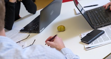 Tre personer arbetar runt ett bord med datorer och papper.