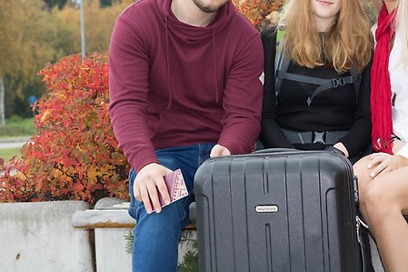 3 elever sitter med en resväska och pass utanför skolan