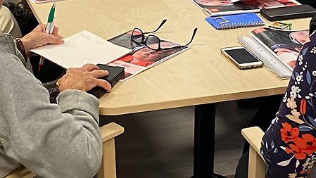 Äldre personer som sitter runt ett bord med mobiltelefoner, block och pennor